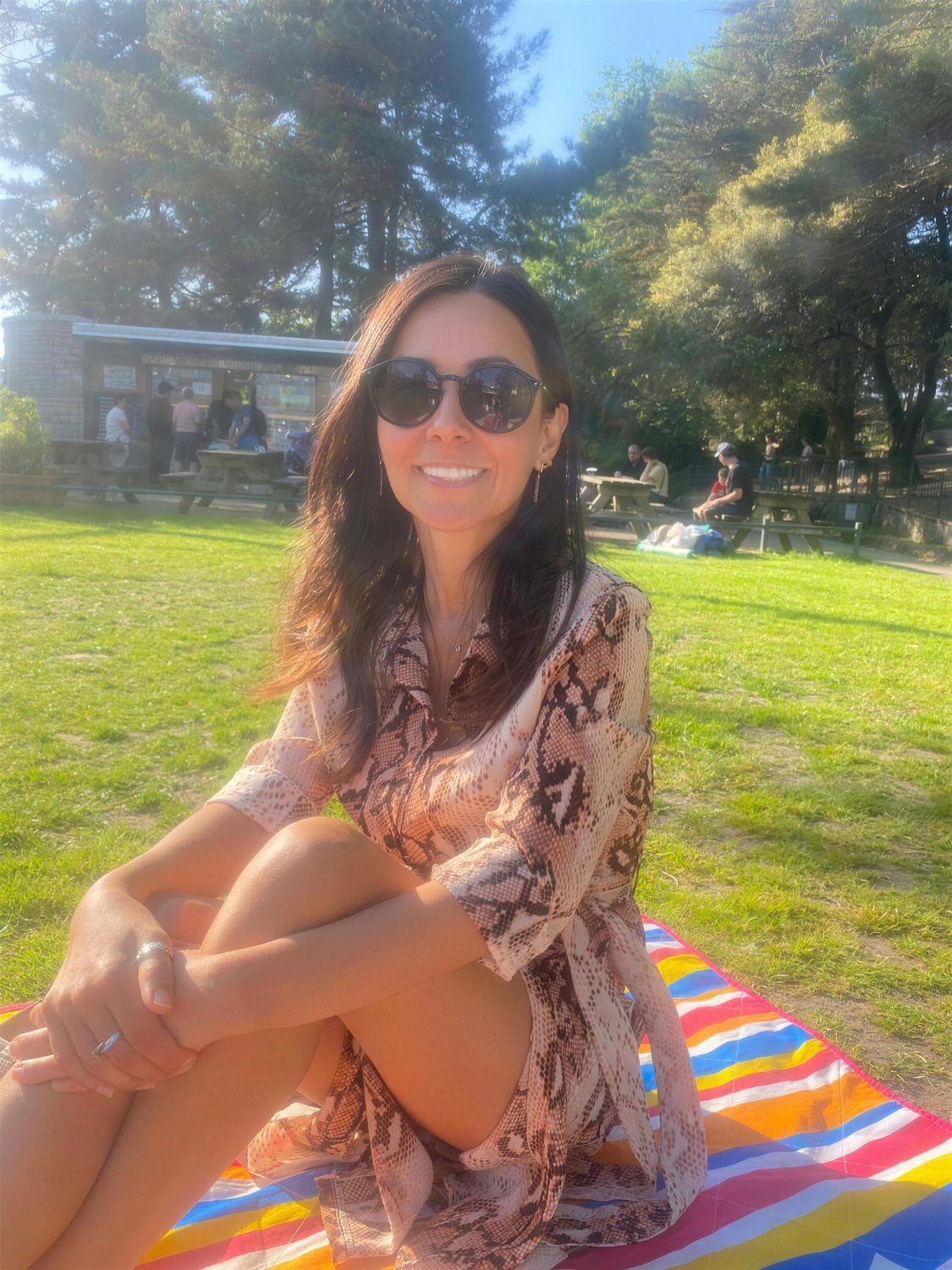Goreti sitting on a picnic blanket in a sunny park.