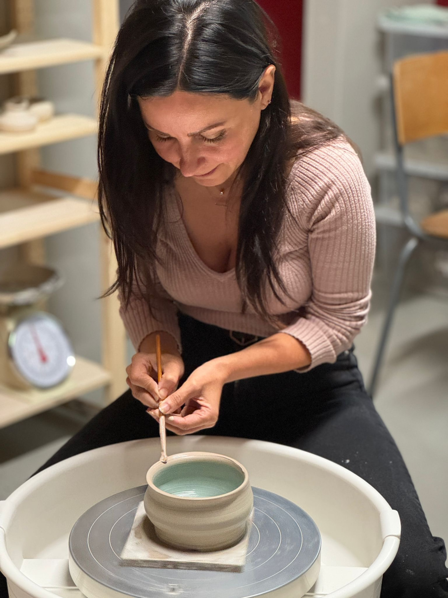 Goreti at a pottery wheel, glazing the inside of a small bowl with a brush.
